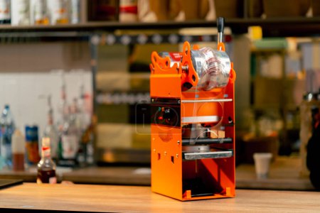 close-up of an orange machine for packaging drinks with plastic on the bar counter