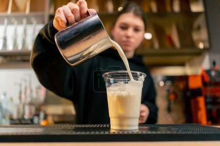 Téléchargez les photos : Gros plan d'une fille mains verser la quantité requise de lait pour un latte dans un verre transparent en plastique - en image libre de droit
