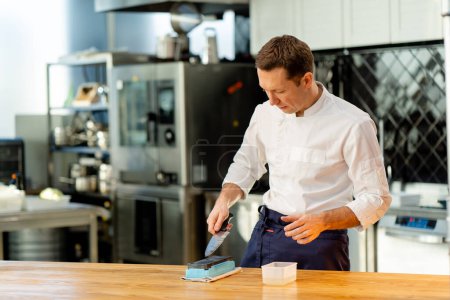 Photo for A chef in a white jacket in the kitchen at the table is preparing a knife on a green plate - Royalty Free Image