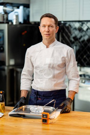 Foto de Un chef en uniforme blanco en la cocina de la mesa está a punto de comprobar la temperatura del producto - Imagen libre de derechos