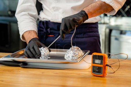Photo for Close-up of a chef in a white uniform in the kitchen at the table getting ready to check the temperature of the product - Royalty Free Image