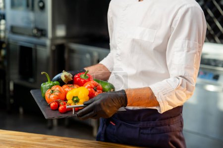 Téléchargez les photos : Gros plan d'un chef tenant un plateau avec différents légumes lavés prêts à l'emploi légumes colorés dans la cuisine - en image libre de droit