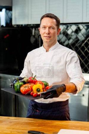 Téléchargez les photos : Chef tenant un plateau avec différents légumes lavés prêts à l'emploi légumes colorés dans la cuisine - en image libre de droit