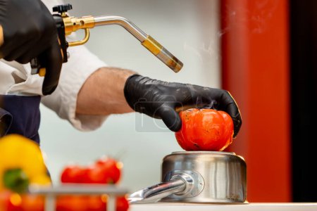 Photo for Close-up, the chef stands in the kitchen wearing black gloves holds a burner and burns a tomato - Royalty Free Image