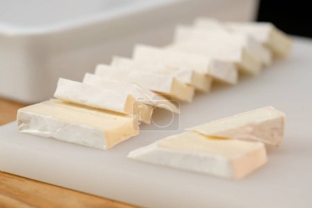 Foto de Primer plano de trozos de queso brie que se encuentran bellamente uno tras otro en una pizarra blanca - Imagen libre de derechos