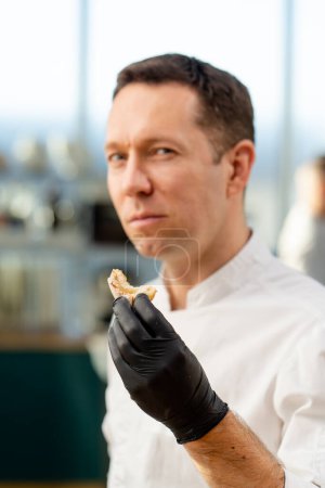 Foto de Primer plano del chef de pie en su cocina en un uniforme blanco sobre la mesa degustación de una baguette en rodajas - Imagen libre de derechos