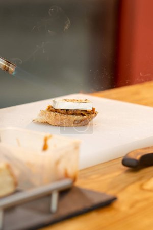 Photo for Close-up of a piece of baguette on the table on a white board burning bread with a torch - Royalty Free Image