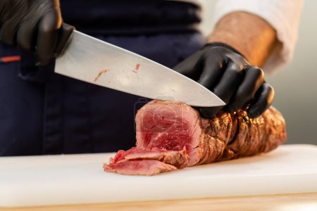 Photo for Close-up of a chefs hands in black gloves cutting a piece of raw jerky meat on a board - Royalty Free Image