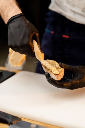Photo for Close-up of a chefs hands in black gloves spreading sauce from a bag onto a piece of baguette - Royalty Free Image
