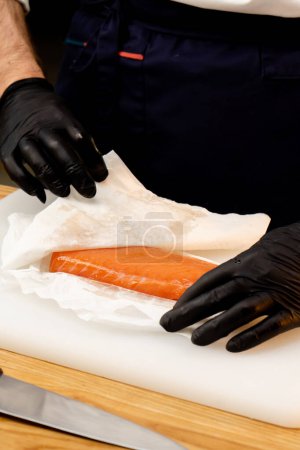 Téléchargez les photos : Gros plan d'un chef mains dans des gants noirs trempant un filet de saumon avec une serviette - en image libre de droit