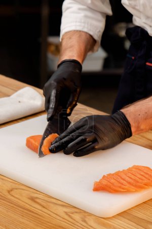 Photo for Close-up of a chefs hands in black gloves cutting salmon fillet on a white board - Royalty Free Image