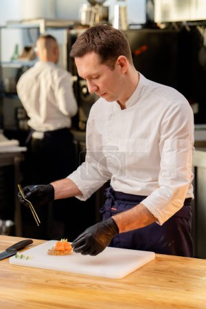 Foto de Las manos en guantes negros colocando un trozo de salmón sobre el pan con pinzas doradas - Imagen libre de derechos