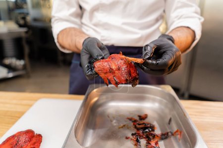 Foto de Primer plano de las manos de un chef en una chaqueta blanca con guantes negros pelando la piel de un pimiento - Imagen libre de derechos