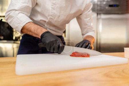 Foto de Primer plano de las manos de un chef en una chaqueta blanca con guantes negros rebanando pimientos - Imagen libre de derechos