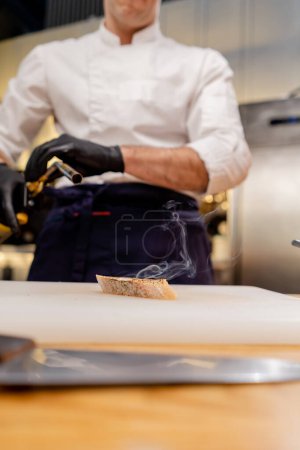 Foto de Primer plano de un pedazo de baguette sobre la mesa sobre una tabla blanca quemando pan con una antorcha - Imagen libre de derechos