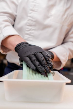 Foto de Primer plano de las manos de un chef en la cocina en una chaqueta blanca que ralla remolachas sobre la mesa - Imagen libre de derechos