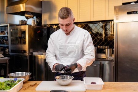 Photo for Assistant chef in the kitchen in a white jacket cuts beets in his hands over the table - Royalty Free Image