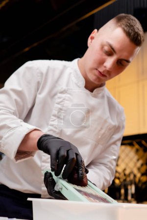 Foto de Primer plano de un chef en la cocina en una chaqueta blanca que ralla remolachas sobre la mesa - Imagen libre de derechos