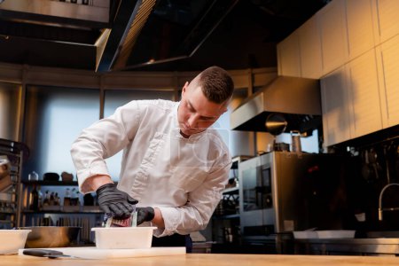 Téléchargez les photos : Un chef dans la cuisine dans une veste blanche grille des betteraves sur une table dans un dollar - en image libre de droit