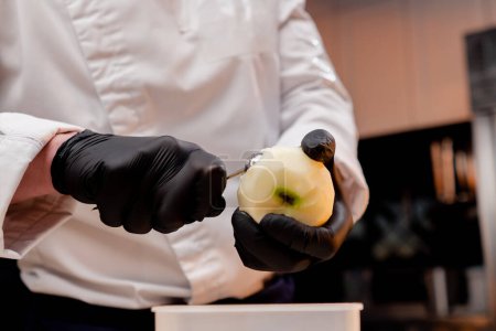 Téléchargez les photos : Gros plan d'un chef dans la cuisine découpant des morceaux ronds d'une pomme pelée jaune - en image libre de droit