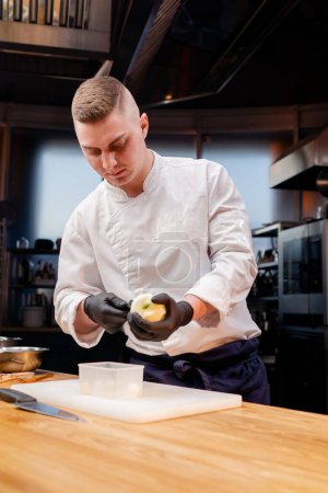Téléchargez les photos : Le chef dans la cuisine de l'établissement coupe des morceaux ronds d'une pomme pelée jaune - en image libre de droit