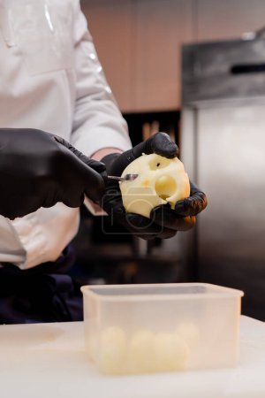 Foto de Primer plano de un chef en la cocina cortando piezas redondas de una manzana pelada amarilla - Imagen libre de derechos