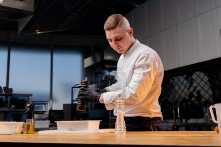 Téléchargez les photos : Un chef en uniforme blanc dans une cuisine professionnelle est sur le point de décaper des betteraves qui se trouvent dans un récipient blanc - en image libre de droit