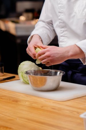 Photo for Close-up of a chefs hand breaking cabbage into an iron plate standing on a white board - Royalty Free Image
