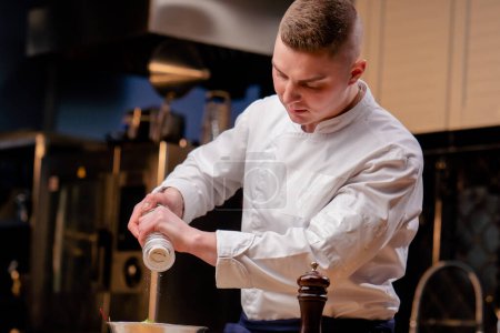 Un chef con uniforme blanco en una cocina profesional saltea una ensalada en un cuenco de metal
