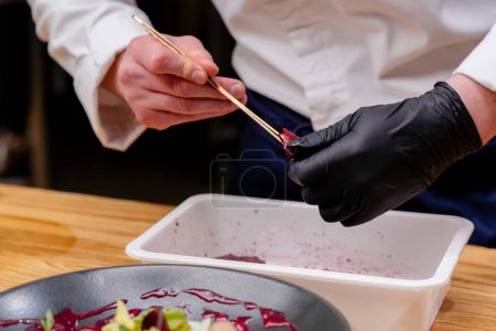 primer plano de un plato negro en el que la ensalada las manos de los chefs le agregan trozos de remolacha con pinzas