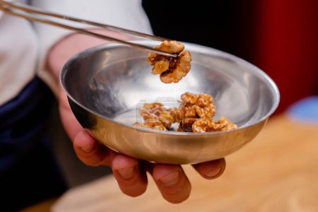 Téléchargez les photos : Gros plan d'un bol de noix et le chef les attrape avec une pince à épiler pour décorer la salade - en image libre de droit