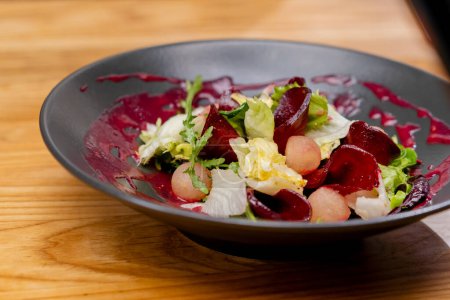 Nahaufnahme auf einem schwarzen Teller mit Salatblättern, Rübenscheiben und runden Apfelstücken