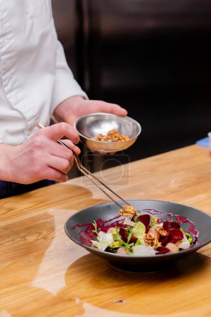 Nahaufnahme einer Schüssel mit Walnüssen und der Koch greift sie mit einer Pinzette, um den Salat auf dem Tisch zu dekorieren