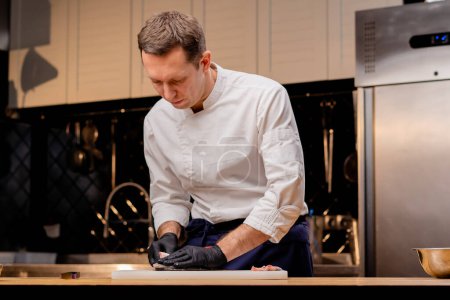 Téléchargez les photos : Un chef vêtu d'une veste blanche dans une cuisine professionnelle coupe le poisson avec un couteau avant de cuisiner - en image libre de droit