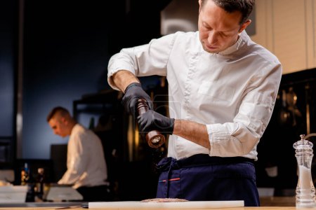 Foto de Chef en una cocina profesional en una chaqueta blanca salazón cortar y cortar pescado - Imagen libre de derechos