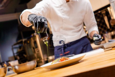 close-up of a chefs hands pouring green sauce from a bottle onto a finished dish