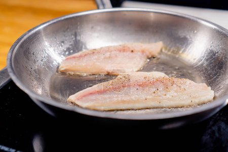 Photo for Close-up of two pieces of transverse fish fillet lying on a professional hot frying pan - Royalty Free Image