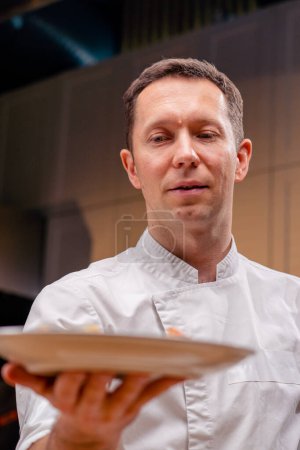 Foto de De cerca la cara del chef demuestra un plato de pescado ya hecho en la longitud de los brazos en una cocina profesional - Imagen libre de derechos
