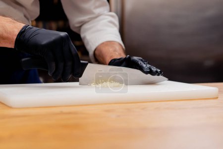 Photo for Close-up of a chefs hands chopping garlic with a large knife on a white board - Royalty Free Image