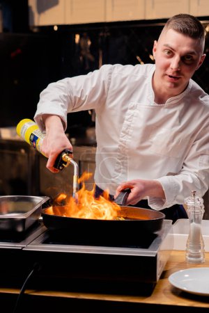 Foto de Un chef freír diferentes verduras en una sartén caliente con una antorcha en la estufa - Imagen libre de derechos