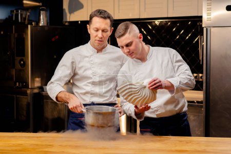 Foto de Dos chefs en uniformes blancos están preparando nitrógeno líquido en la cocina que se extiende por toda la mesa - Imagen libre de derechos