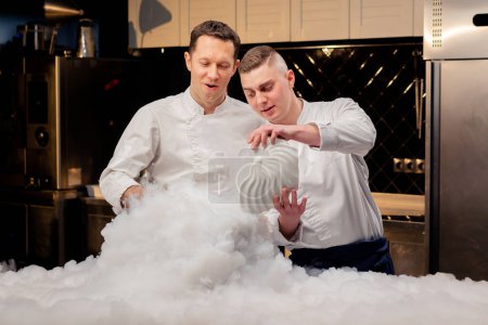 Foto de Dos chefs en uniformes blancos están preparando nitrógeno líquido en la cocina que se extiende por toda la mesa - Imagen libre de derechos
