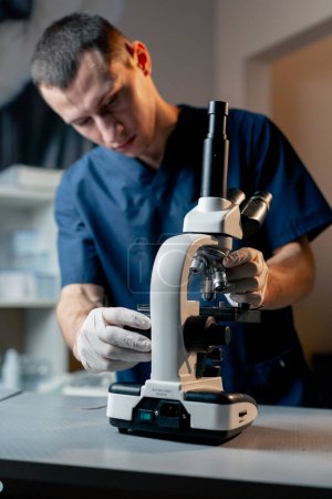 Téléchargez les photos : Dans une clinique vétérinaire, un jeune médecin ajuste la grossièreté au microscope - en image libre de droit
