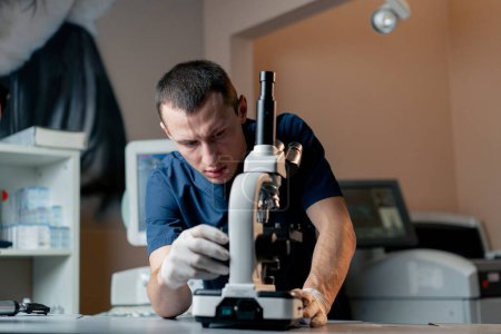 Foto de En una clínica veterinaria un médico joven ajusta la grosería en un microscopio - Imagen libre de derechos