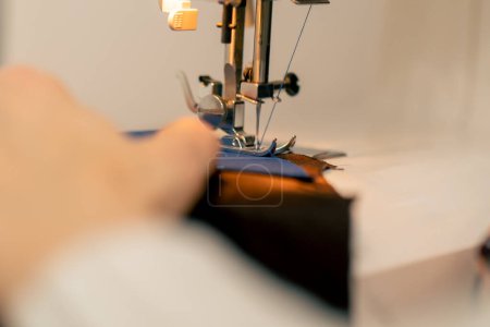 Foto de Primer plano en un taller de costura en una máquina el maestro costurera hace un corte en una tela azul - Imagen libre de derechos