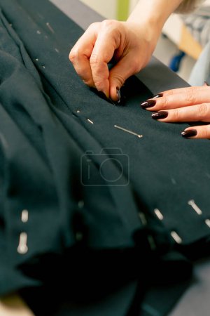 close up in a sewing workshop seamstress pins a corrugated pin on a black fabric