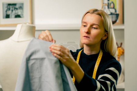 in a sewing workshop seamstress works with a mannequin and pins blue fabric with a pin