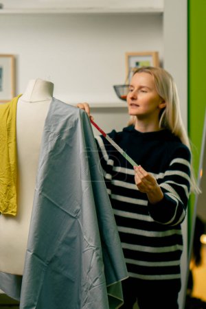 Foto de En un taller de costura una costurera trabaja con un maniquí sobre un tejido azul mide con un centímetro - Imagen libre de derechos