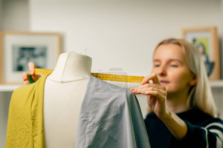 Photo for In a sewing workshop a seamstress works with a mannequin on a blue fabric measures with a centimeter - Royalty Free Image