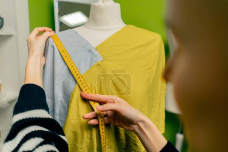 Photo for Close up in a sewing workshop a seamstress works with a mannequin on a blue fabric measures with a centimeter - Royalty Free Image